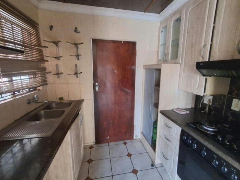 A functional kitchen featuring built-in cabinetry, double sink, gas hob with extractor, and tiled finishes, offering potential for modernization.