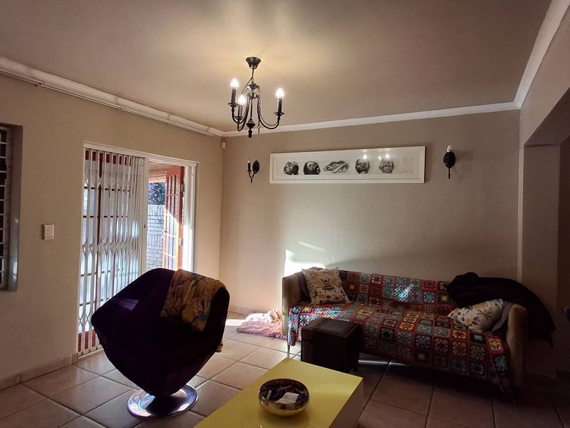 A living room featuring tiled flooring, a chandelier, and a sliding security gate leading to the exterior.