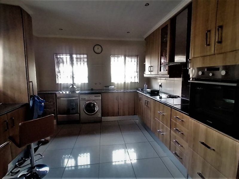 A functional kitchen featuring wooden cabinetry, granite countertops, built-in oven, extractor fan, and tiled flooring with ample natural light.