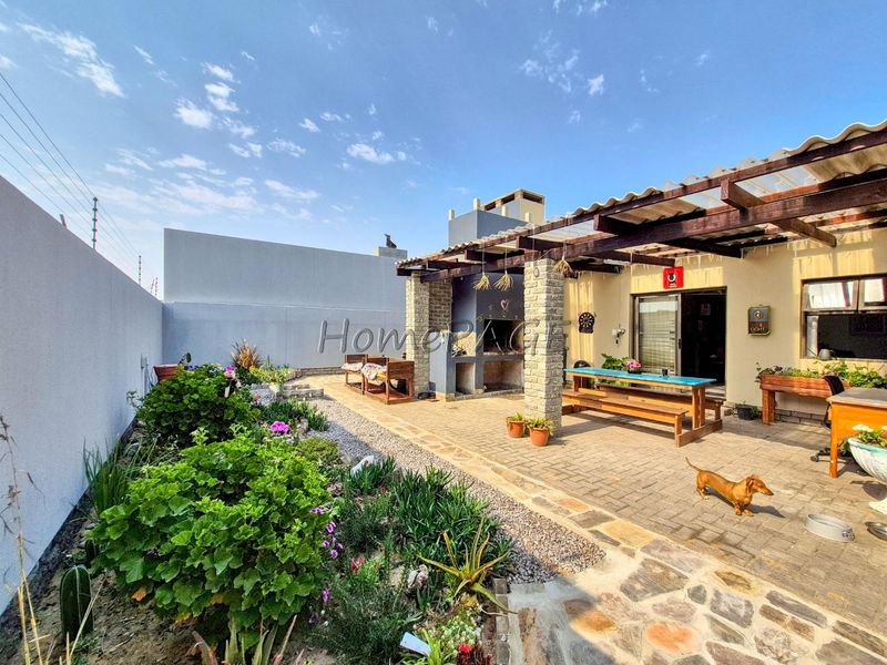Outdoor patio area featuring a built-in braai, timber pergola structure, and paved flooring, set within a private garden space.
