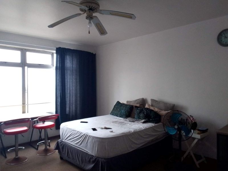 A bedroom featuring a ceiling fan and large window, providing natural light and a functional layout for a comfortable living space.