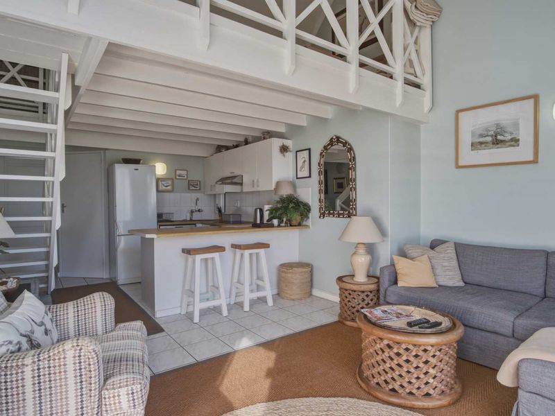 Open plan living area featuring a compact kitchen with breakfast bar, tiled flooring, and a mezzanine level accessed by a staircase.
