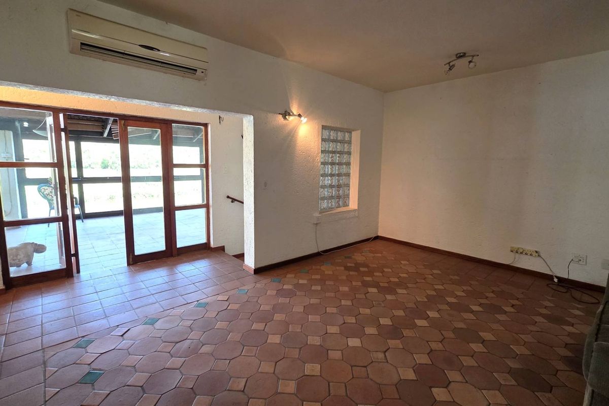 Spacious living area featuring terracotta tile flooring, a unique glass block window, and direct access to an outdoor patio through wooden framed glass doors.