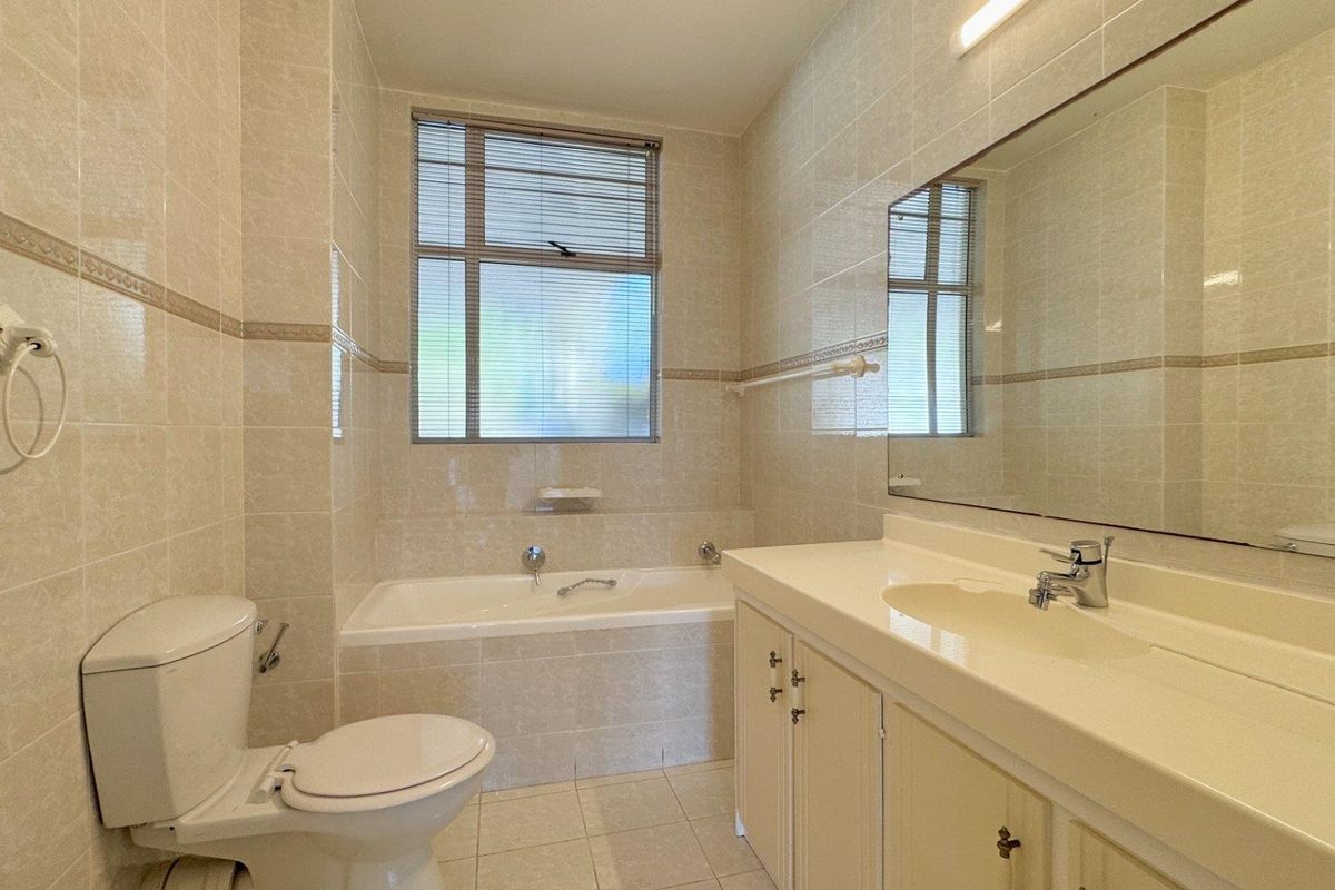 A clean, functional bathroom featuring a built-in bathtub, vanity cabinet with integrated sink, large wall mirror, and neutral floor-to-ceiling wall tiles.