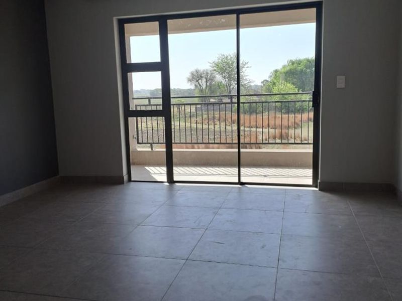 An empty living room featuring large sliding glass doors that open onto a balcony with scenic outdoor views and modern tiled flooring.