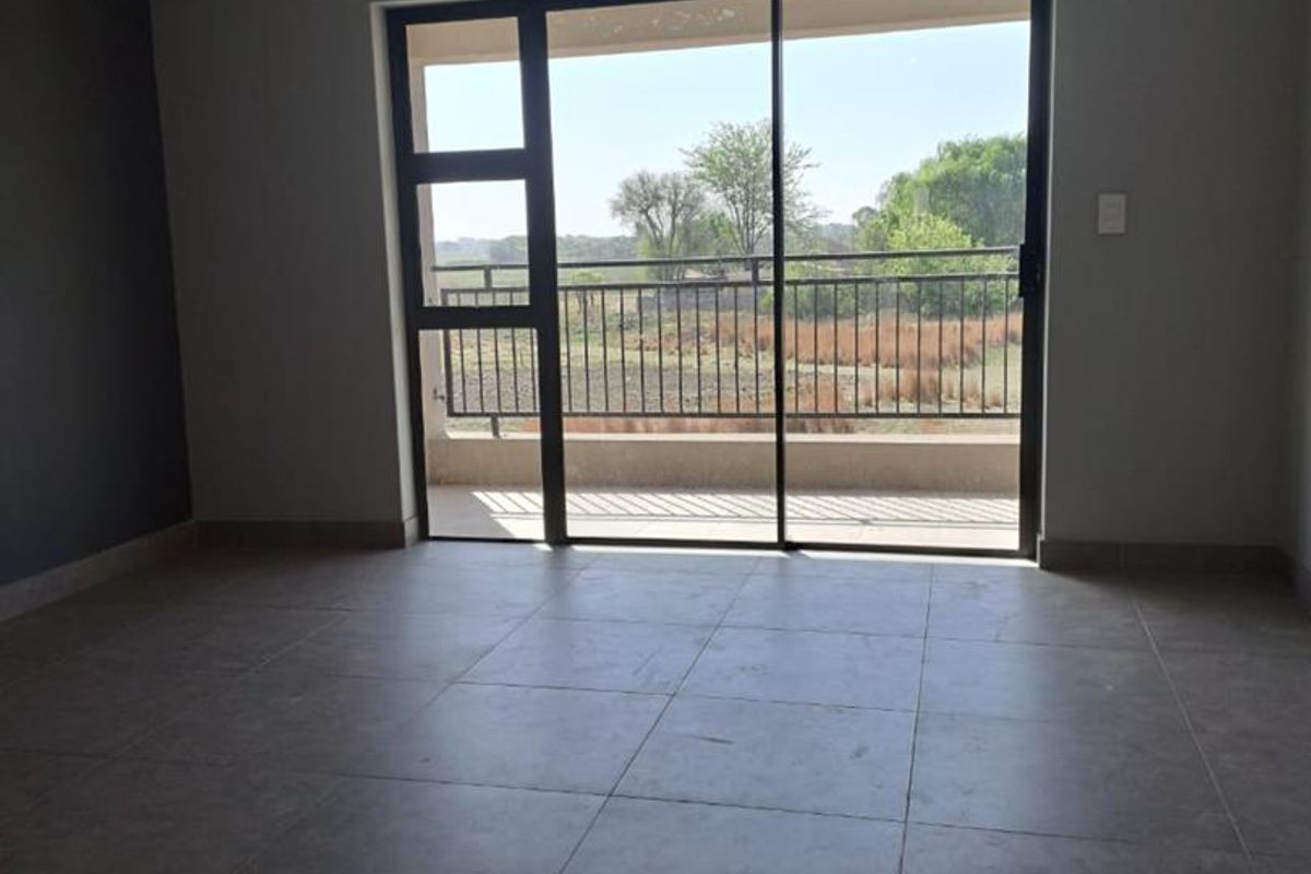 An empty living room featuring large sliding glass doors that open onto a balcony with scenic outdoor views and modern tiled flooring.