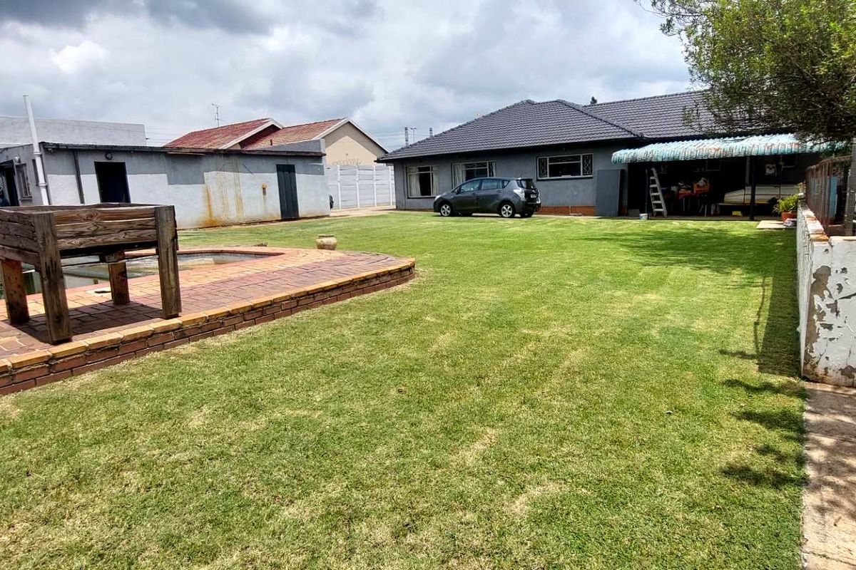 Spacious rear garden featuring a lawn area, paved pool surround, and a covered patio attached to the main house structure.