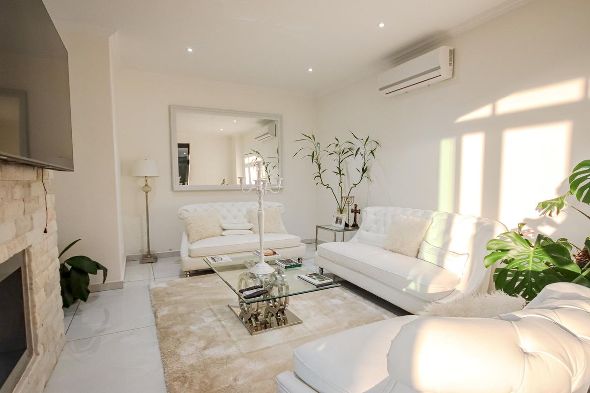 A bright and modern living room featuring a stone-clad fireplace, recessed ceiling lighting, and a wall-mounted air conditioning unit.