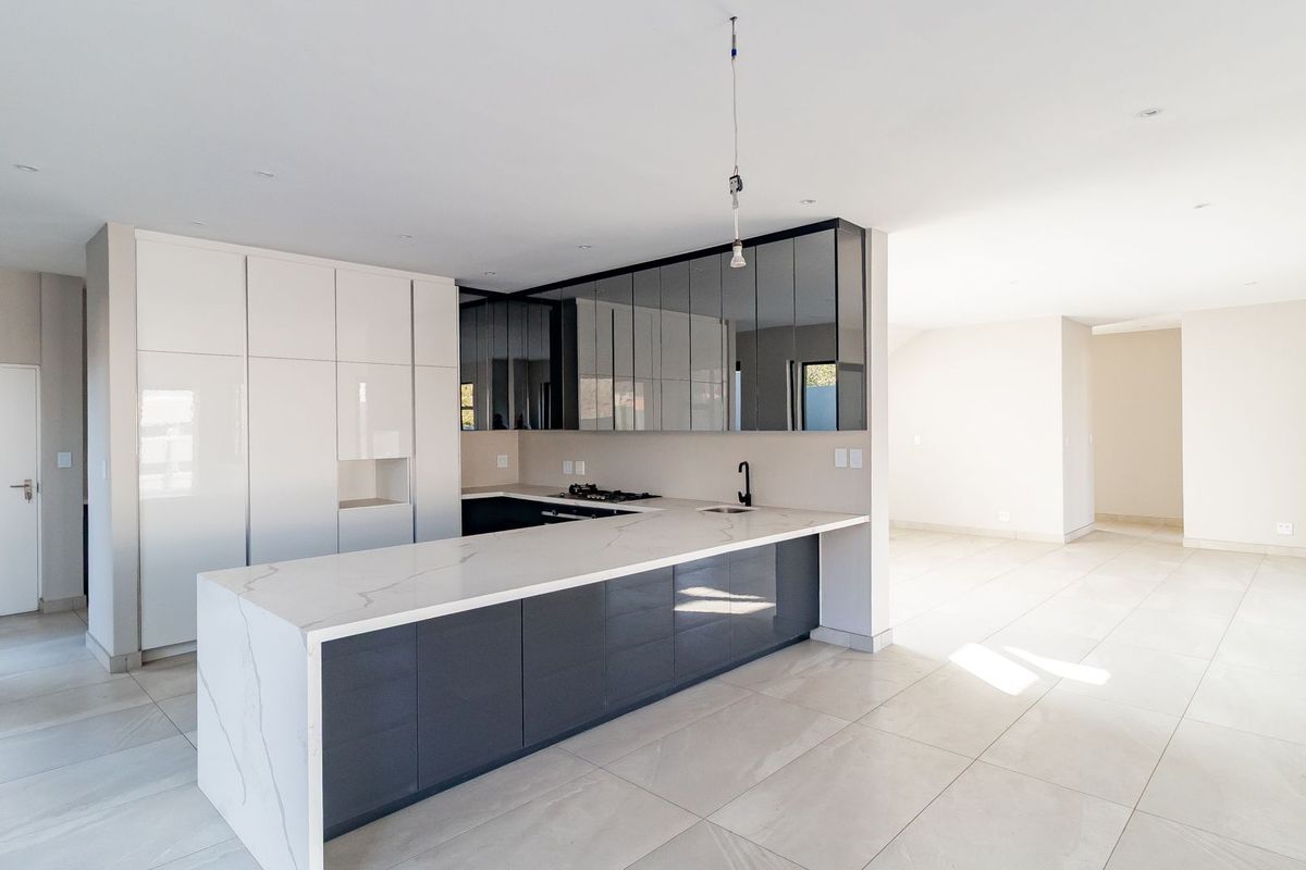Modern open-plan kitchen featuring high-gloss cabinetry, stone countertops, integrated appliances, and sleek tiled flooring in a bright, spacious layout.