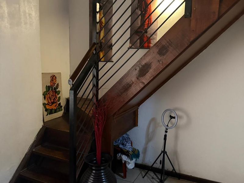 A hallway featuring a wooden staircase with a modern metal balustrade and tiled flooring.