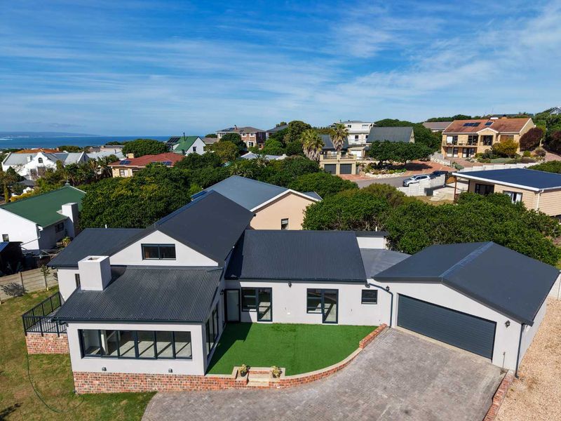 Aerial view of a modern residential property featuring a dark corrugated metal roof, double garage, paved driveway, and a well-maintained artificial lawn area.