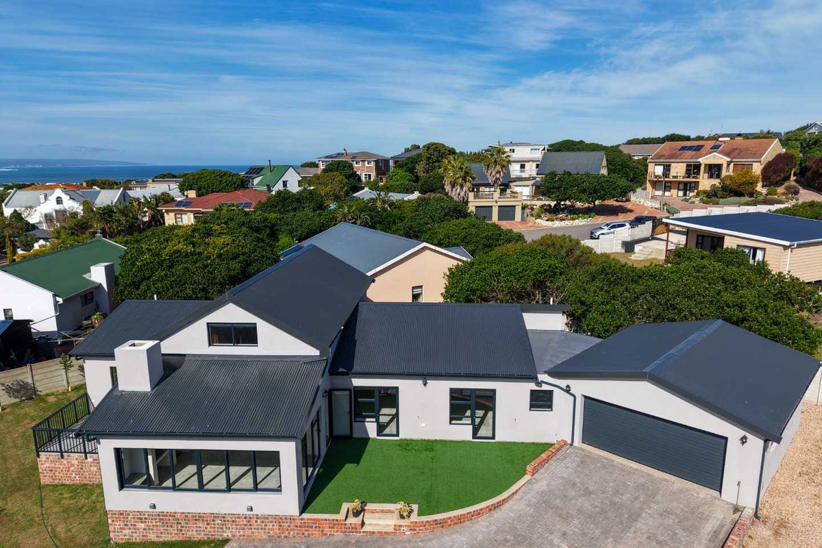Aerial view of a modern residential property featuring a dark corrugated metal roof, double garage, paved driveway, and a well-maintained artificial lawn area.