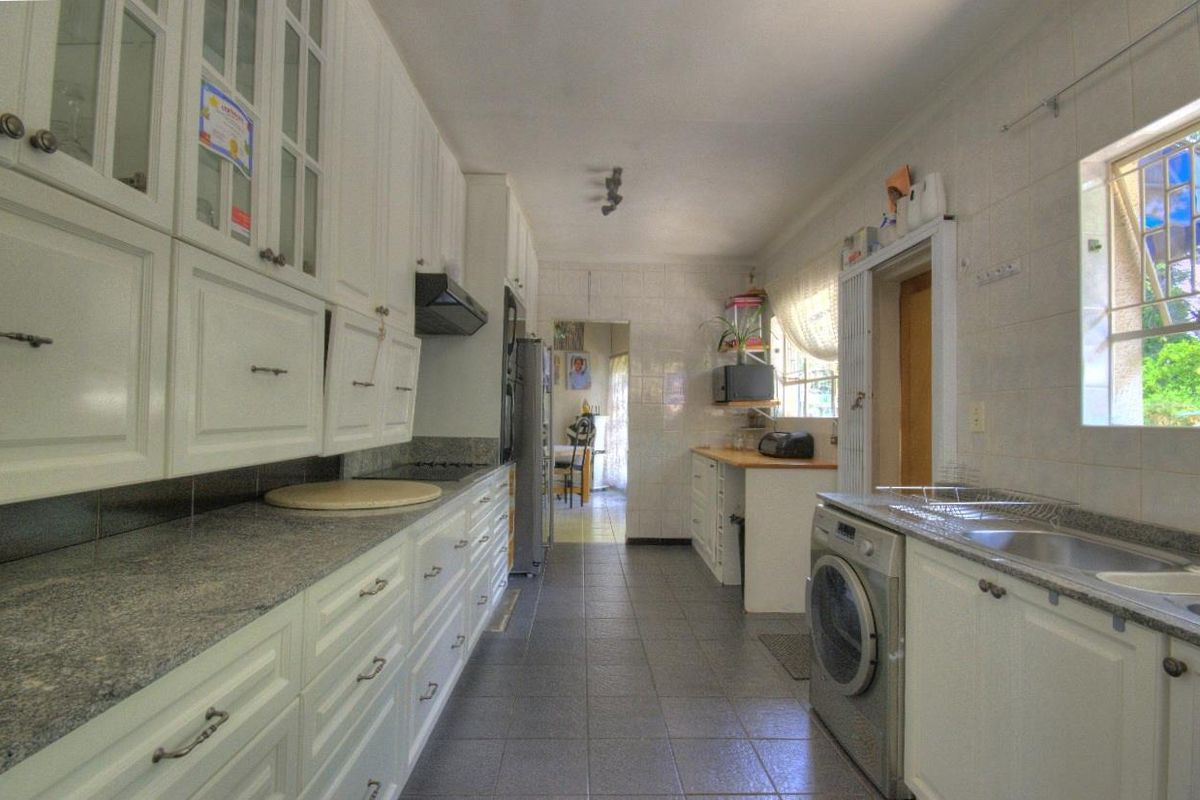 A functional kitchen featuring white cabinetry, granite countertops, tiled walls, and integrated laundry facilities, offering a clean and practical workspace.