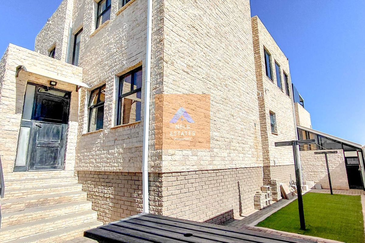 Exterior view of a multi-story townhouse featuring stone cladding, a raised entrance with stairs, and a small side garden area.