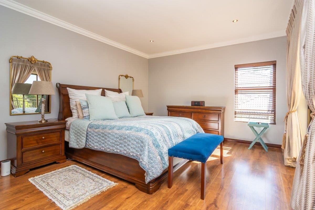 A well-maintained bedroom featuring laminate flooring, crown molding, and recessed lighting, with natural light provided by a window fitted with venetian blinds.