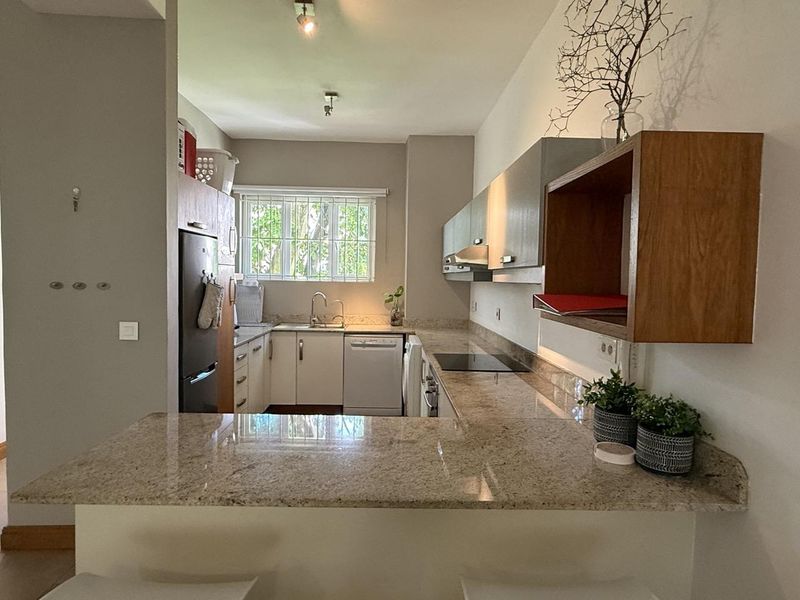 A functional kitchen featuring granite countertops, ample built-in cabinetry, an electric hob, extractor fan, and an integrated dishwasher with a breakfast bar area.