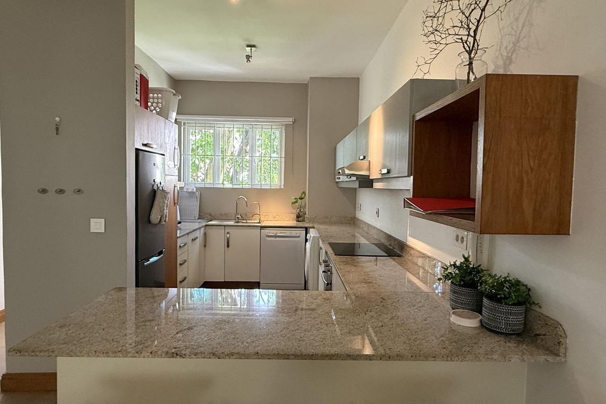 A functional kitchen featuring granite countertops, ample built-in cabinetry, an electric hob, extractor fan, and an integrated dishwasher with a breakfast bar area.