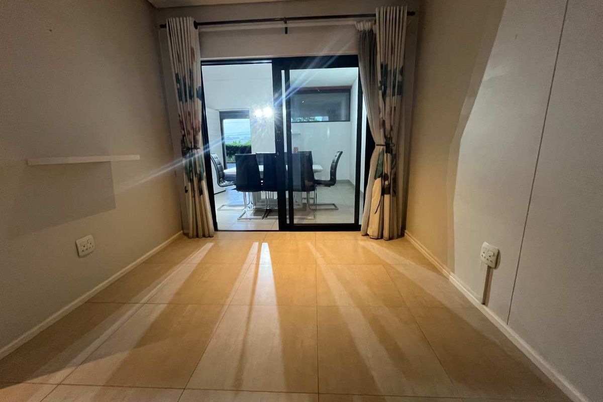 An empty living area featuring large format floor tiles and a sliding glass door providing access to an outdoor dining space.