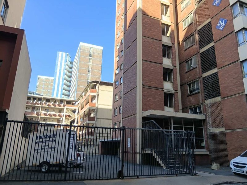 Exterior view of a multi-story brick apartment building featuring a gated entrance, concrete staircase, and decorative breeze block detailing.