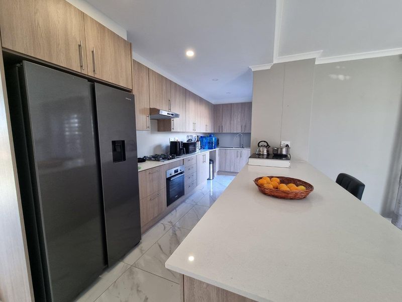 Modern kitchen featuring light wood cabinetry, stone countertops, a central island, and integrated appliances with polished tiled flooring.