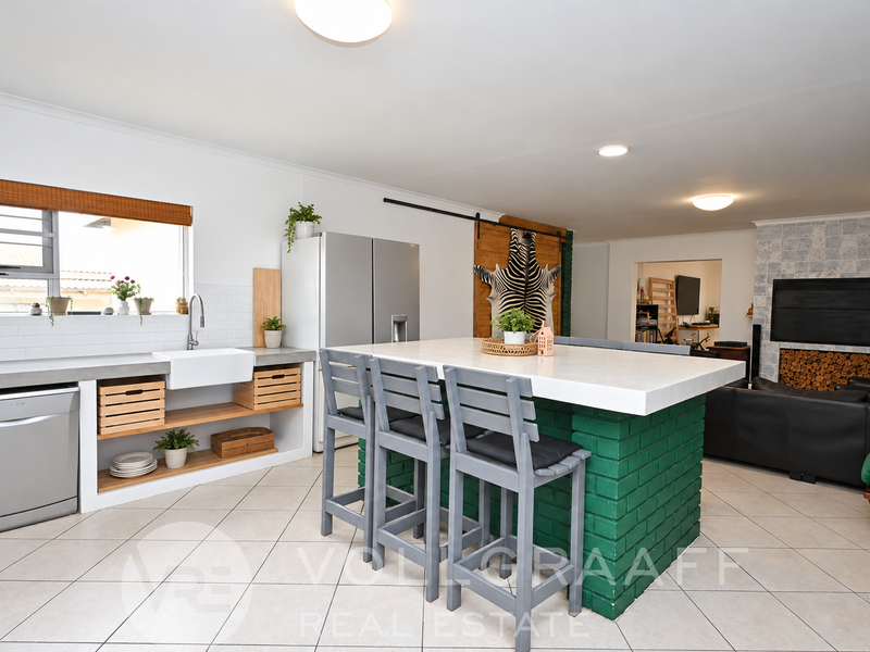 Spacious open-plan kitchen and living area featuring a large island, farmhouse sink, tiled floors, and a built-in fireplace with a decorative tiled surround.