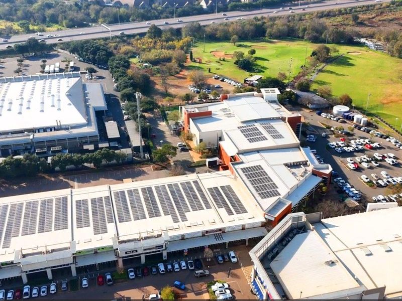 Aerial view of a commercial office complex featuring extensive rooftop solar panel installations, ample parking facilities, and surrounding landscaped green space.
