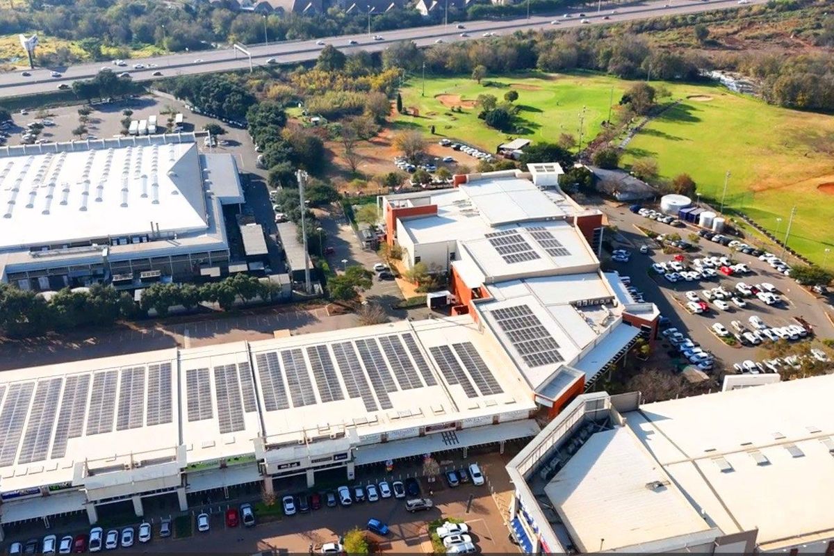 Aerial view of a commercial office complex featuring extensive rooftop solar panel installations, ample parking facilities, and surrounding landscaped green space.