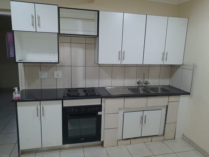 A functional kitchen featuring white cabinetry, a black countertop, built-in oven and hob, and a double sink with tiled backsplash.