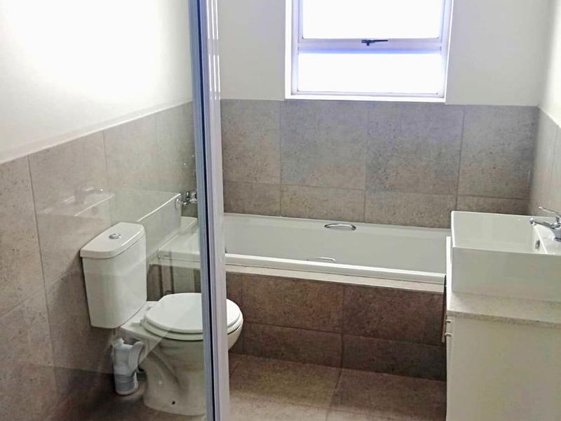 A clean, modern bathroom featuring a bathtub, a separate shower enclosure, a vanity with a basin, and neutral floor-to-ceiling tiling.