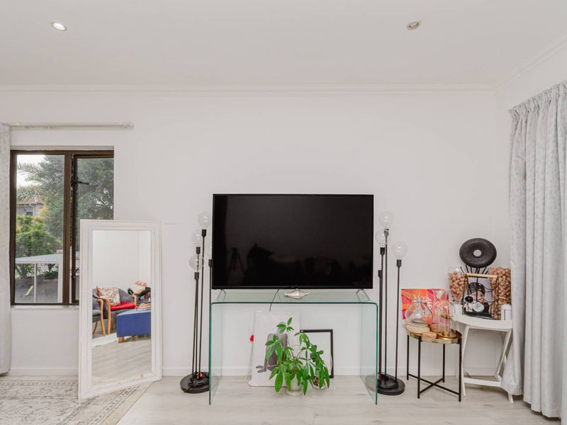A bright living room featuring recessed downlights, neutral walls, and large windows with curtain tracks, providing a clean and functional space.