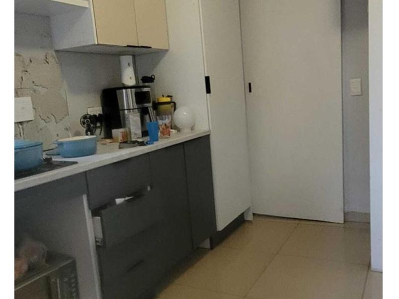 Compact kitchen area featuring built-in cabinetry, tiled flooring, and a sliding door, currently showing signs of wear and requiring cosmetic updates.