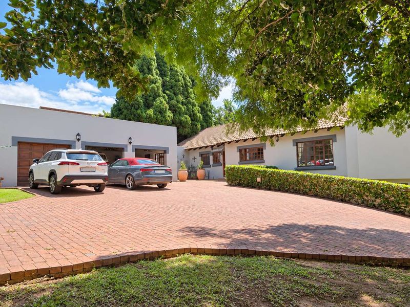 A well-maintained front exterior featuring a spacious paved driveway, a double garage, and a neatly landscaped hedged garden area.