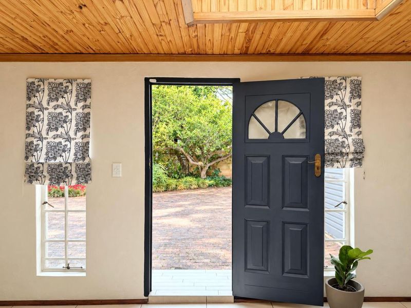 Bright entrance hall featuring a timber ceiling, tiled flooring, and a classic panelled front door opening onto a paved garden area.