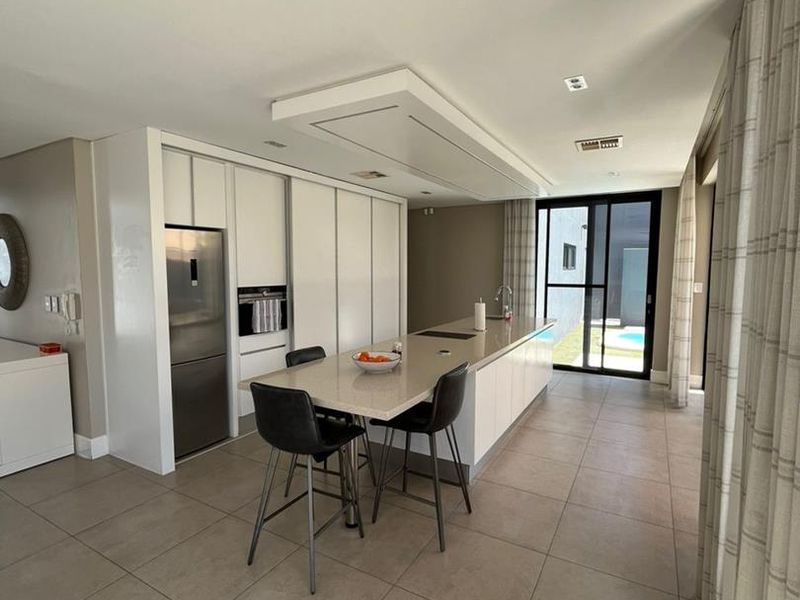 Modern kitchen featuring a large central island with stone countertops, integrated appliances, sleek cabinetry, and direct access to the outdoor pool area.
