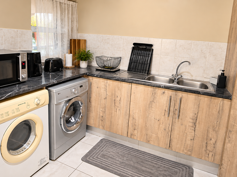 Functional scullery featuring laminate cabinetry, double bowl stainless steel sink, tiled backsplash, and dedicated space for laundry appliances.