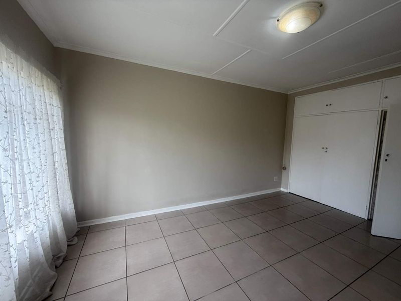 A clean, empty bedroom featuring neutral tiled flooring, built-in cupboards, and a simple ceiling light fixture, offering a blank canvas for personalization.
