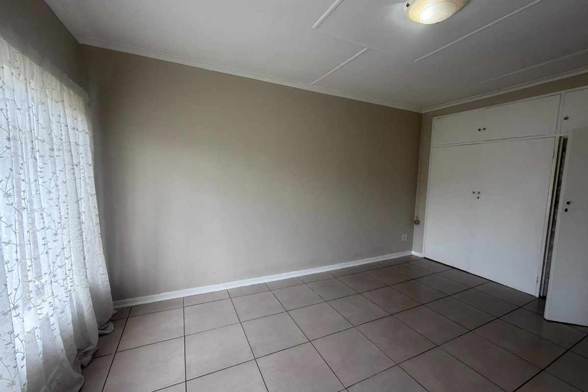 A clean, empty bedroom featuring neutral tiled flooring, built-in cupboards, and a simple ceiling light fixture, offering a blank canvas for personalization.