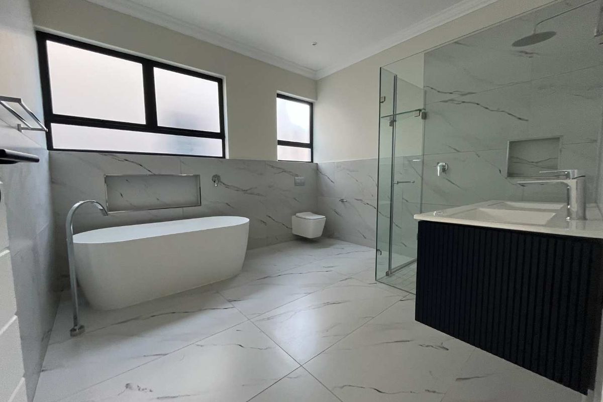 Modern bathroom featuring a freestanding bathtub, wall-mounted toilet, glass-enclosed shower, and a sleek floating vanity with marble-look tiling throughout.