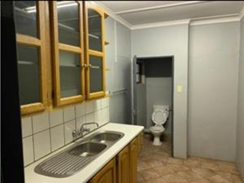 A functional scullery area featuring built-in cabinetry, a double stainless steel sink, and an adjoining toilet, requiring cosmetic updates to modernize the space.