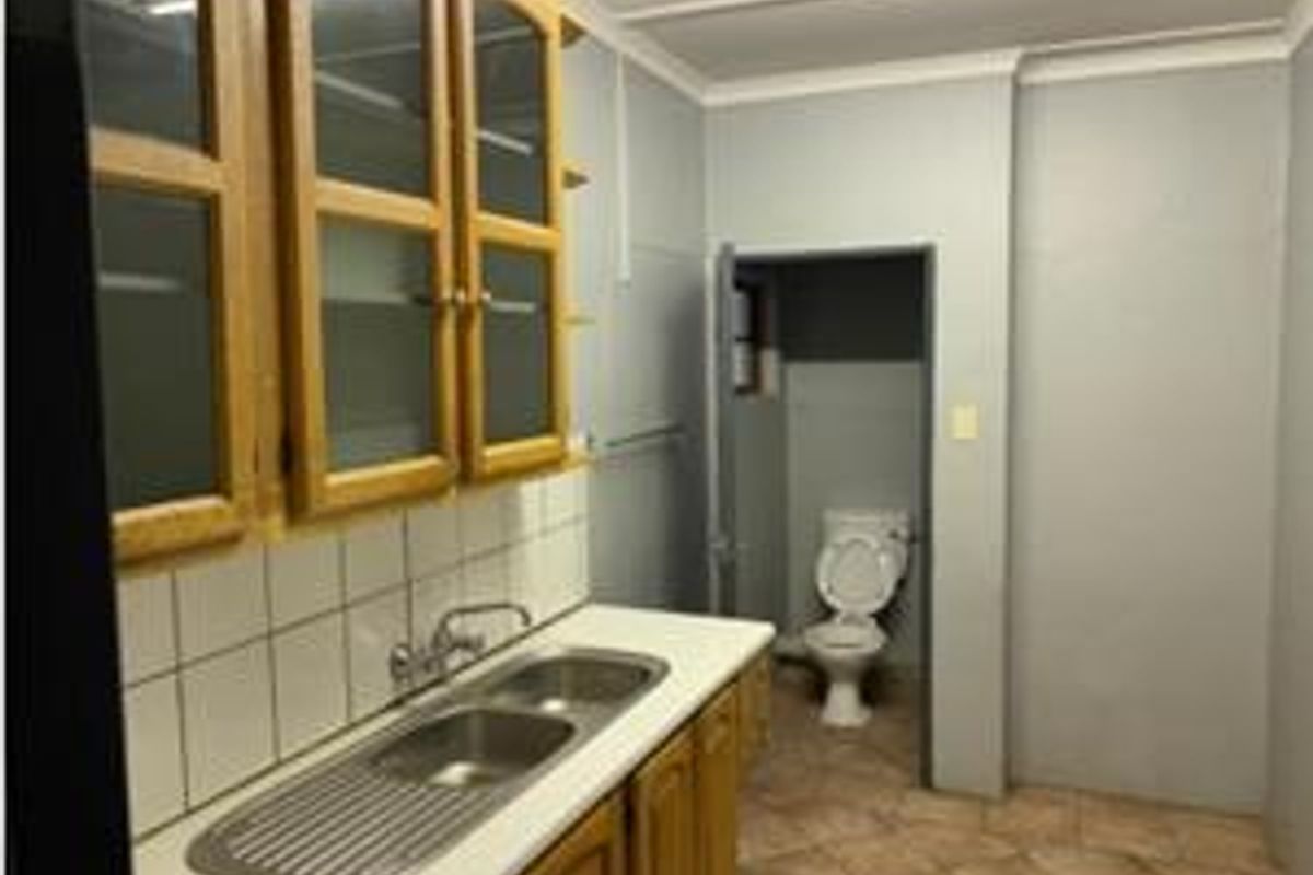 A functional scullery area featuring built-in cabinetry, a double stainless steel sink, and an adjoining toilet, requiring cosmetic updates to modernize the space.