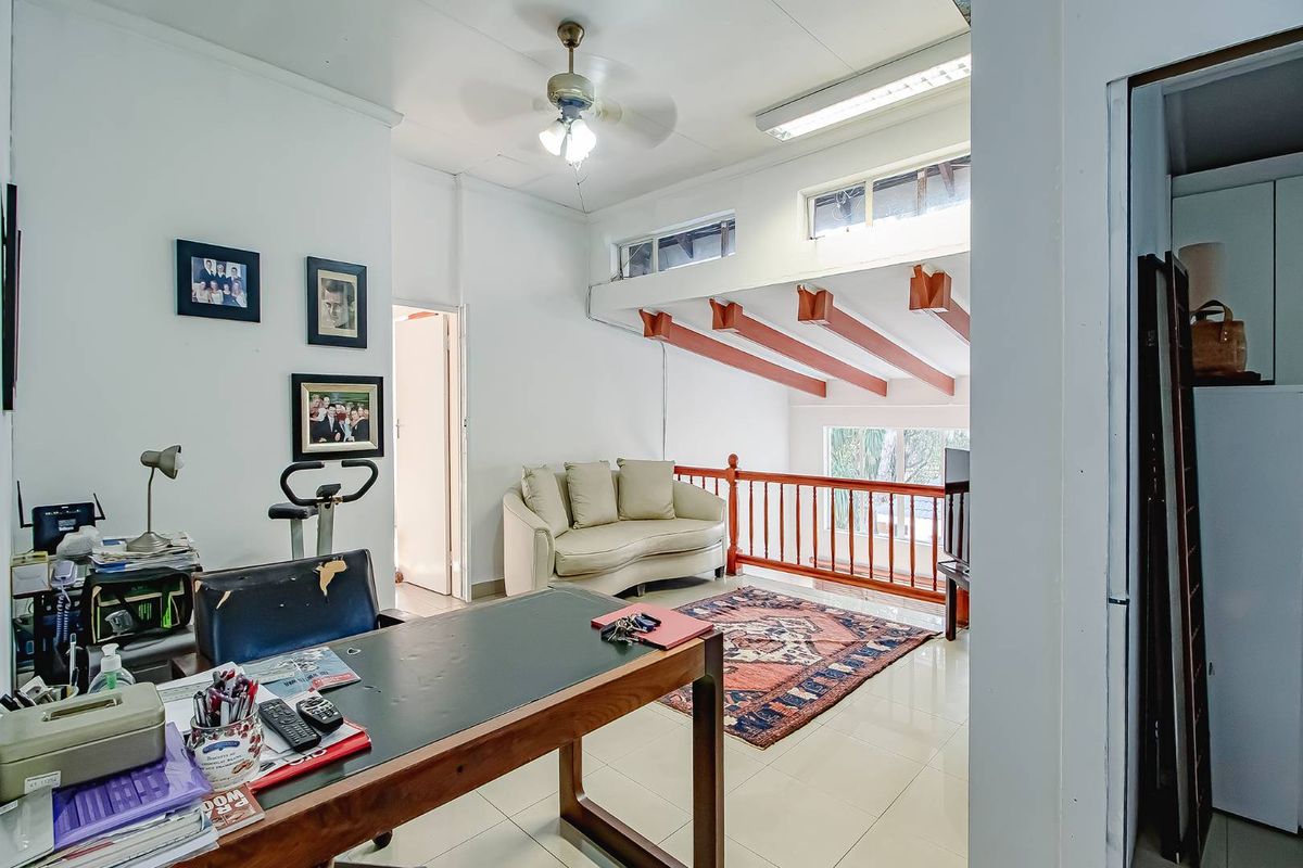A multi-purpose living area featuring a mezzanine-style layout with exposed timber beams, tiled flooring, and a wooden balustrade overlooking the lower level.