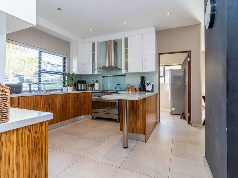 Modern kitchen featuring wood-grain lower cabinetry, white upper cabinets, stone countertops, stainless steel appliances, and a glass splashback with tiled flooring.