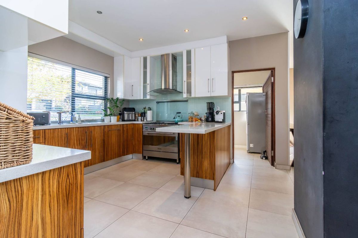Modern kitchen featuring wood-grain lower cabinetry, white upper cabinets, stone countertops, stainless steel appliances, and a glass splashback with tiled flooring.