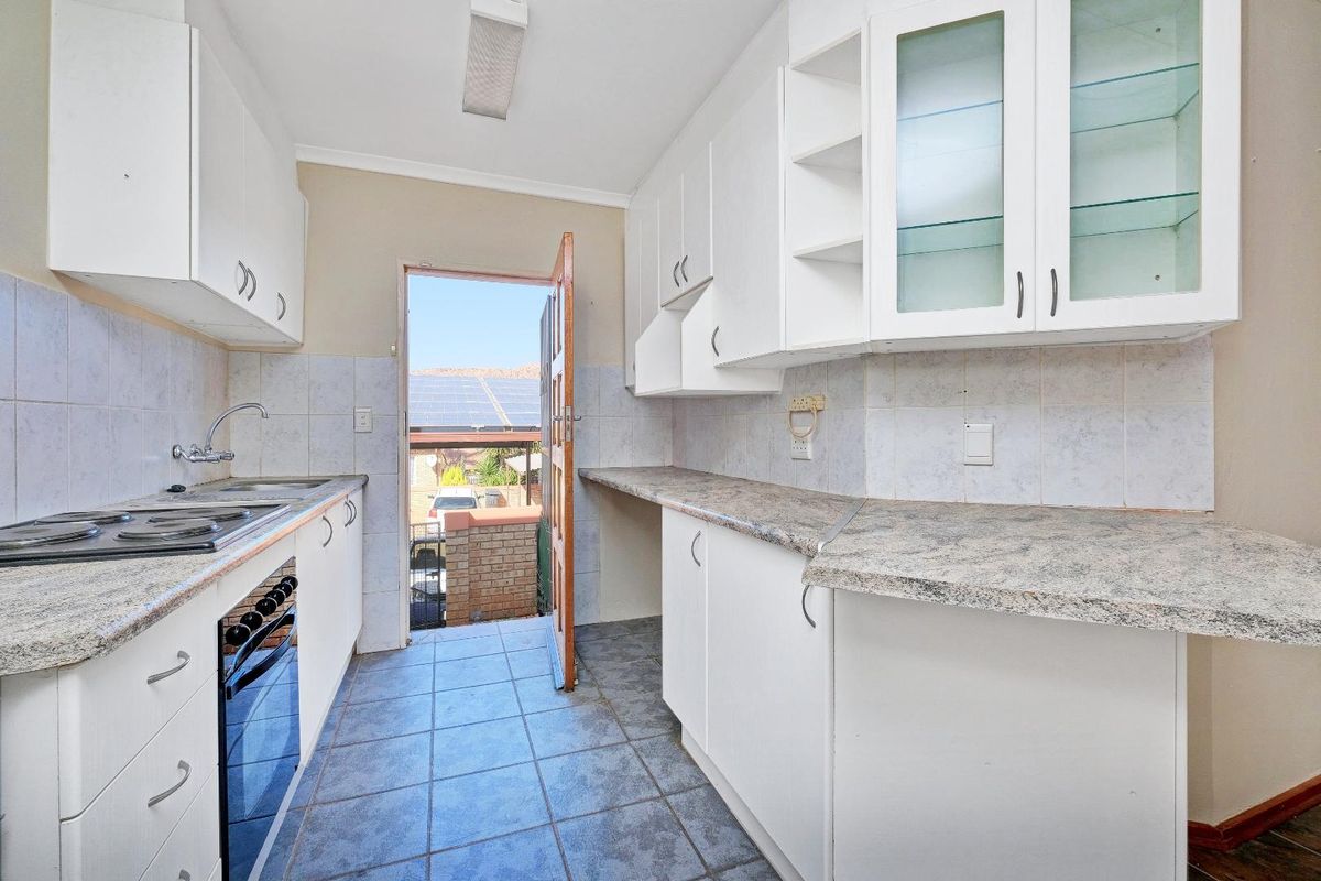 Functional kitchen featuring white cabinetry, stone-look laminate countertops, integrated oven and hob, and direct access to the exterior.