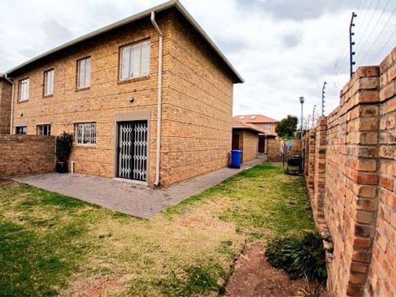 Rear view of a face brick townhouse featuring a paved patio area, enclosed garden with perimeter walling, and security fencing.