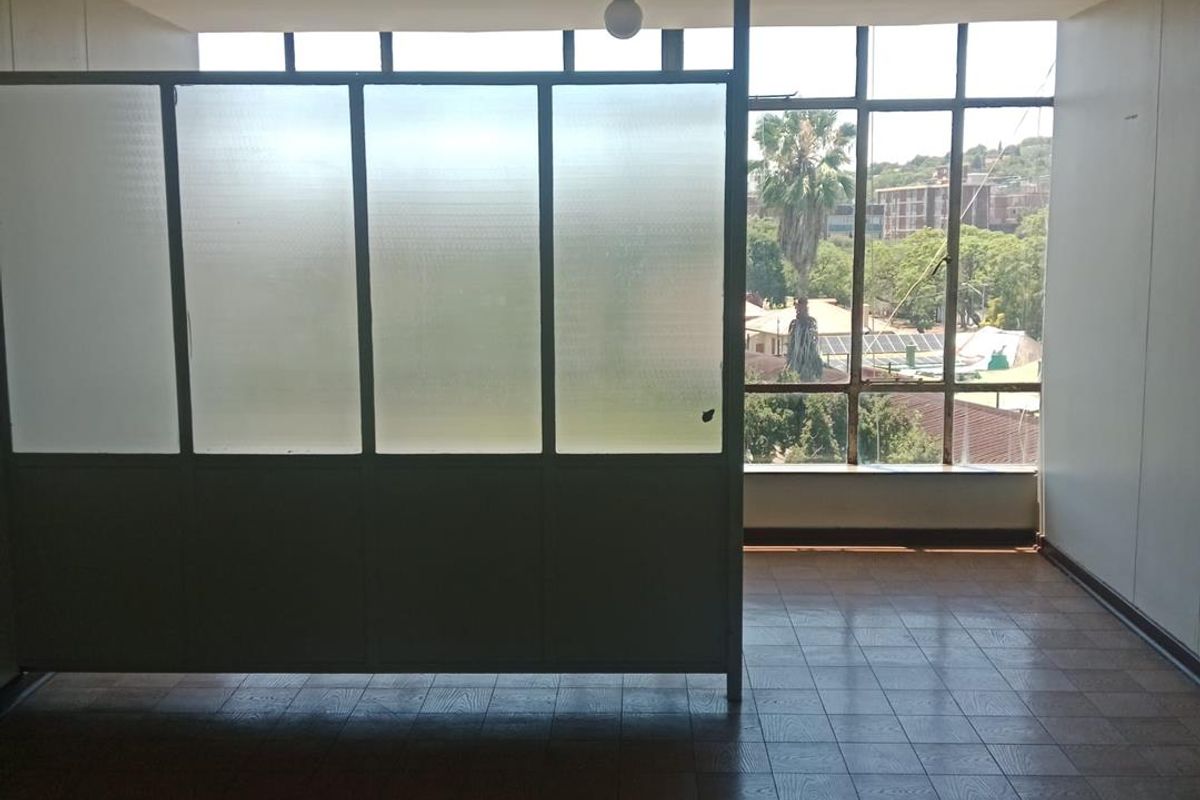 An empty living area featuring large windows with neighborhood views and a frosted glass partition, offering a blank canvas for renovation.