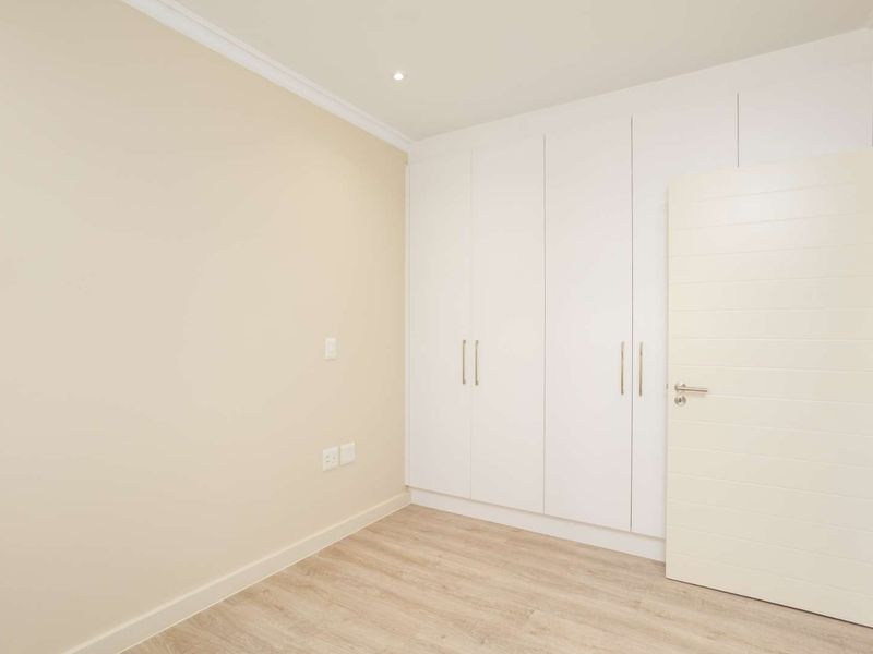 A clean, empty bedroom featuring modern built-in cupboards, light laminate flooring, and recessed downlighting, offering a neutral canvas for personalization.