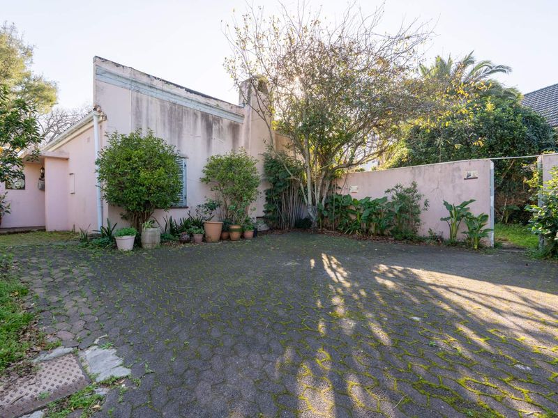 Front exterior view of the property featuring a paved driveway, perimeter boundary wall, and established garden elements.