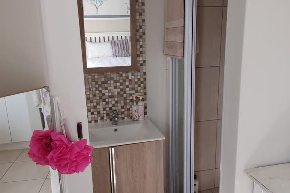 Compact bathroom featuring a vanity cabinet with basin, mosaic tile backsplash, and a separate shower enclosure with tiled flooring.