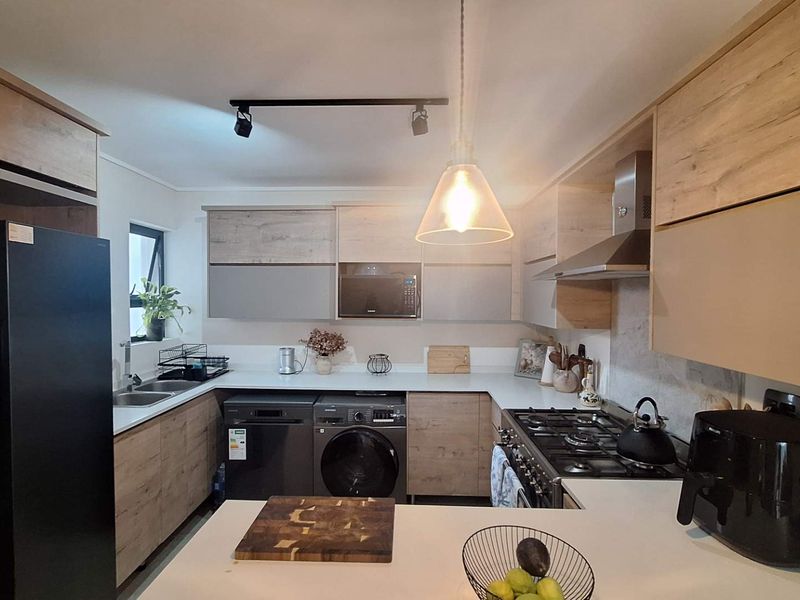 Modern kitchen featuring light wood-tone cabinetry, stone countertops, gas hob, extractor fan, and integrated appliances in a functional U-shaped layout.